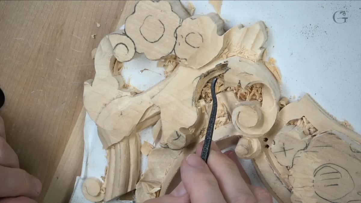 Dark undercut tool working behind a scroll with pencil layout marks still on the wood