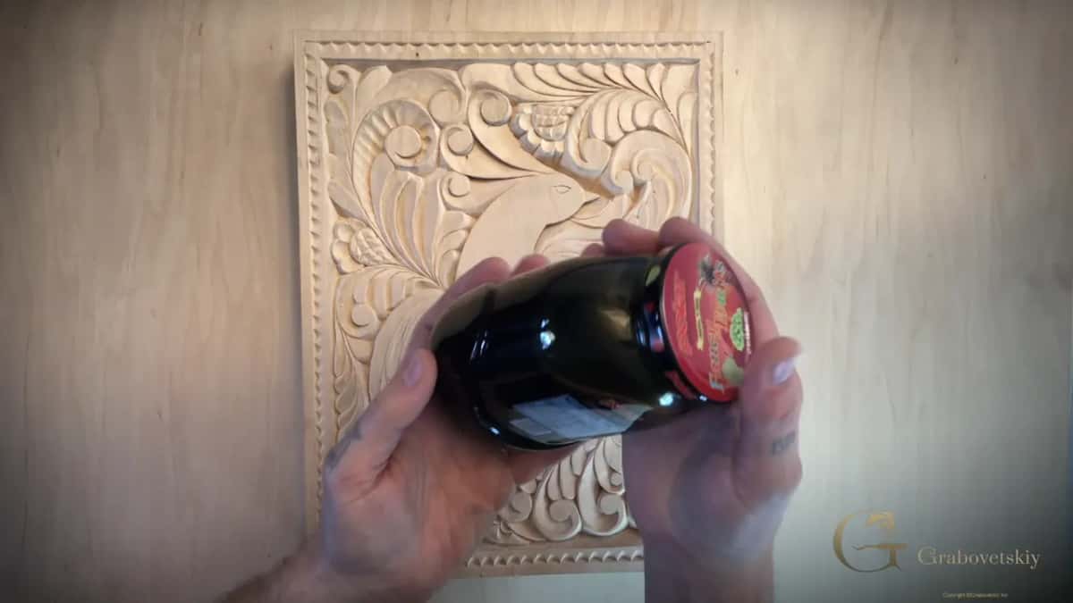 Jar of dark stain held over the bare carved panel