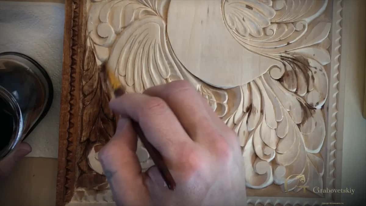 Thin brush working dark stain into the hollows down the left side of the bird panel