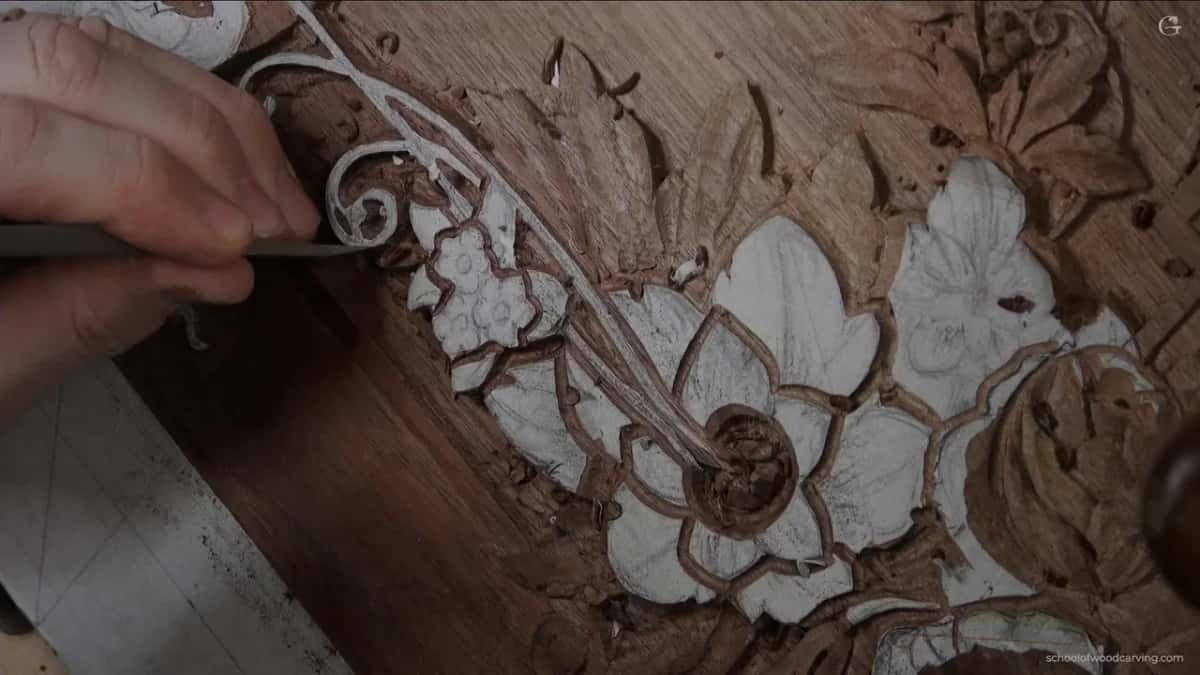 Hand and gouge above the carved scroll, with loose chips lying on the walnut.