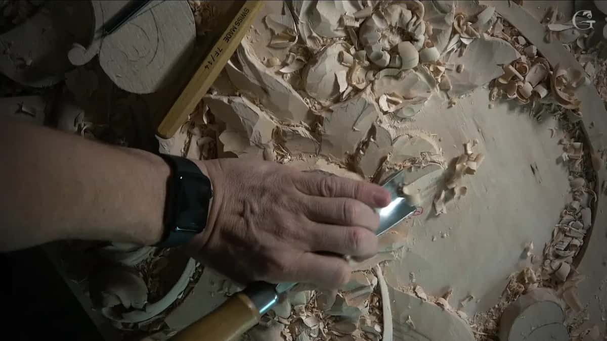 Palm pressing a wide gouge almost flat against a sloped leaf, shavings piled all around it