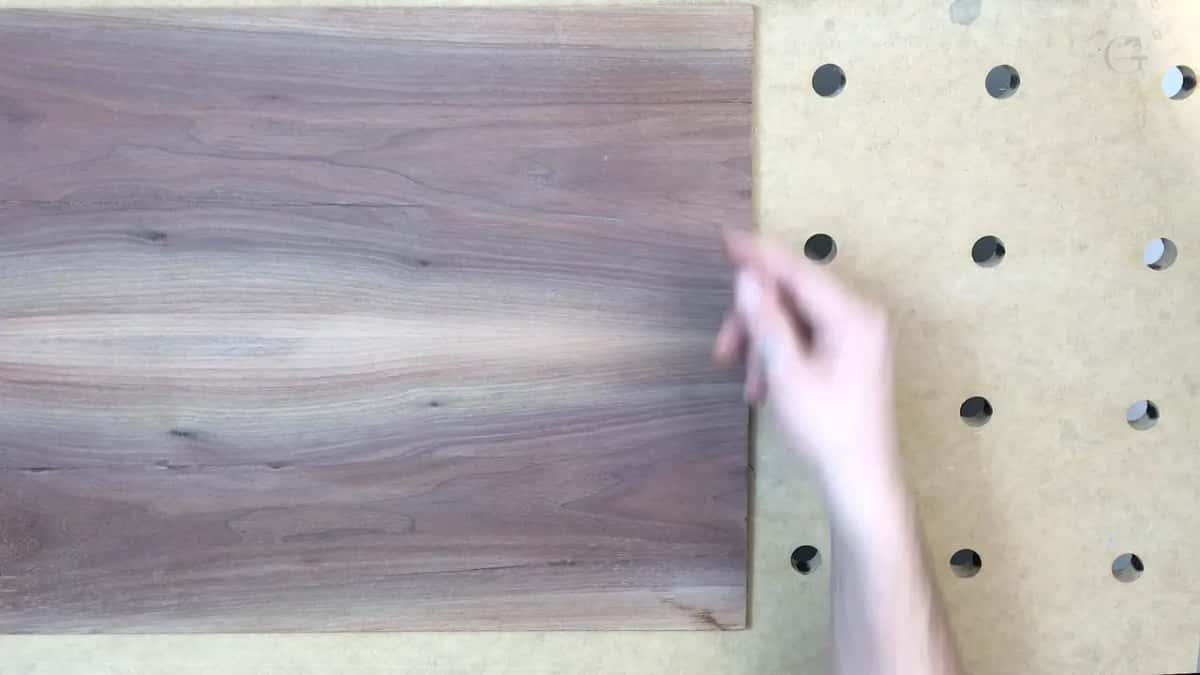 A hand reaches the short side of the walnut, the drilled bench board beside it