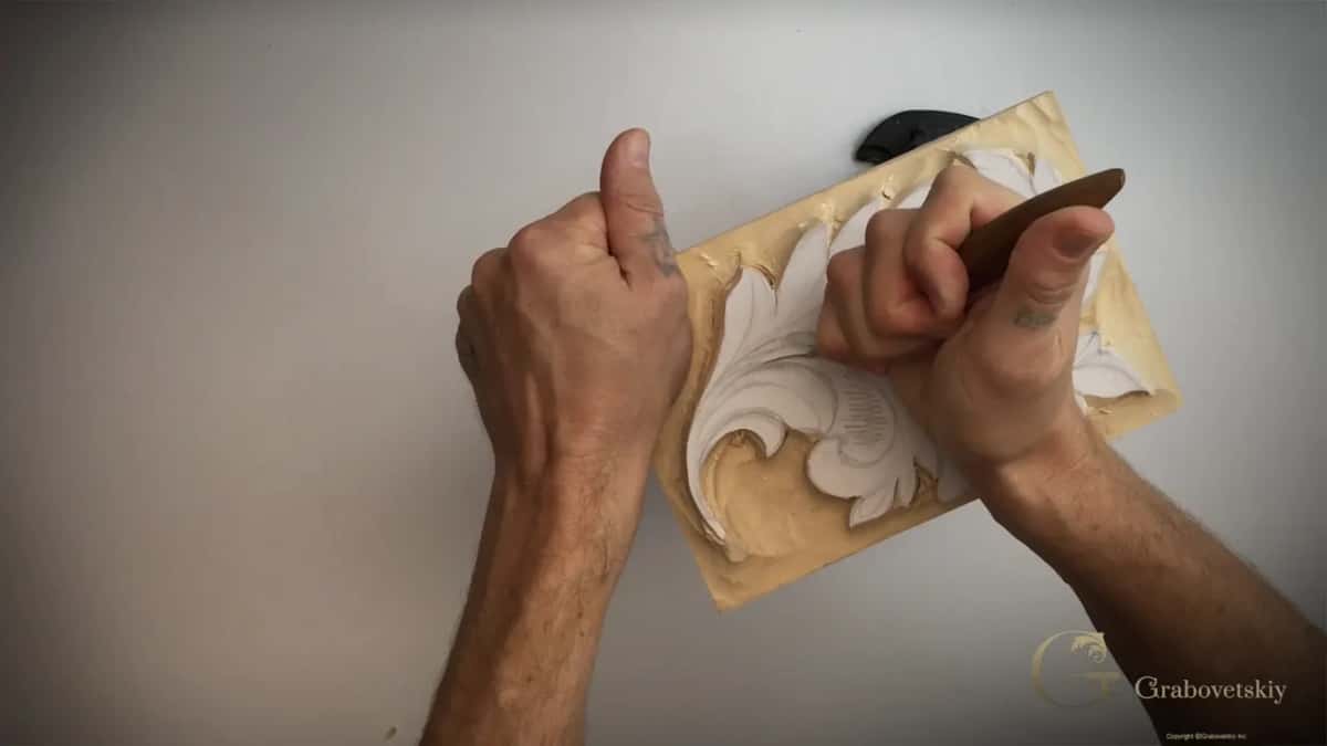 Both hands down on the panel, the right one gripping the knife low near the bottom of the leaf