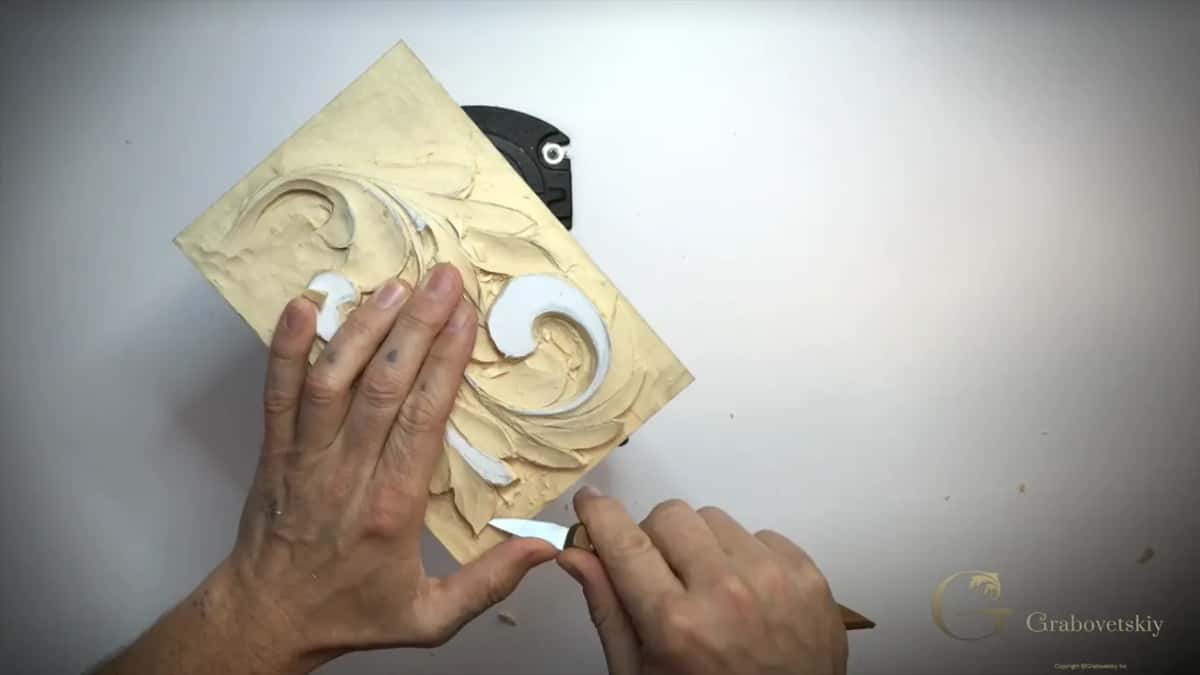 Small knife by the lower edge, fingers spread across the carving