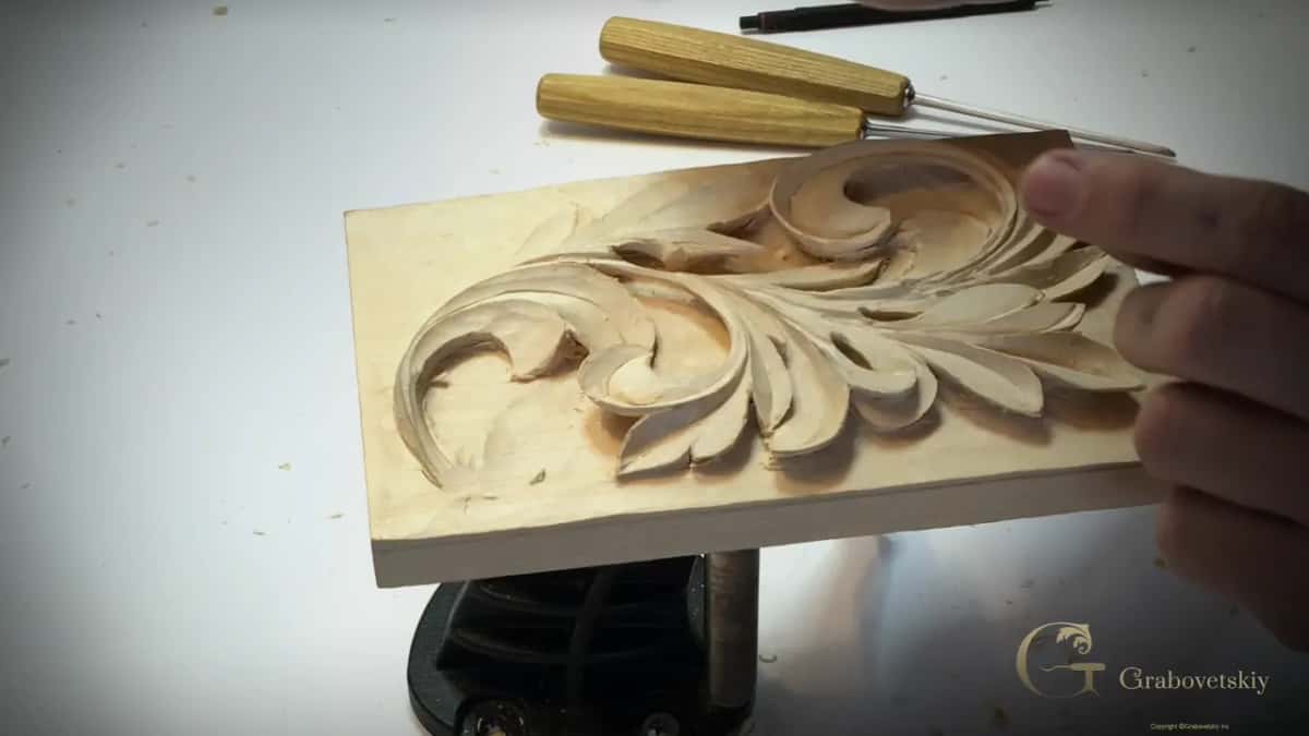 Two gouges rest beyond the board as a hand steadies its right edge