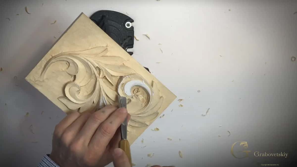 A gouge in the right fist with its edge set into the curl, chips scattered on the white table
