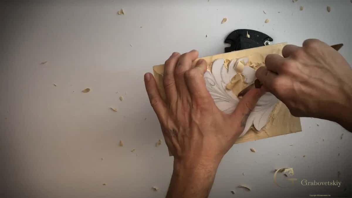 Knife held low in a pocket while a curl of waste lifts, the other hand flat on the panel