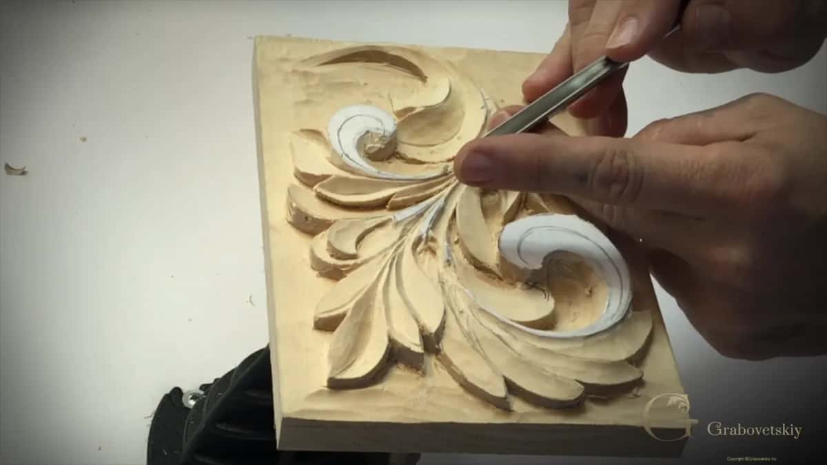 V tool laid across two fingers, its edge working near the upper curl
