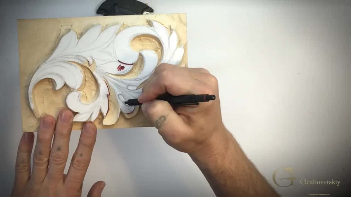 Left hand spread on the table below the panel while a black marker touches the lower right of the leaf