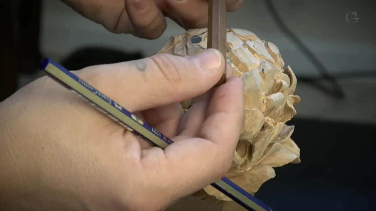 Blue pencil across one palm, the same hand pinching a brown tool against the flower.