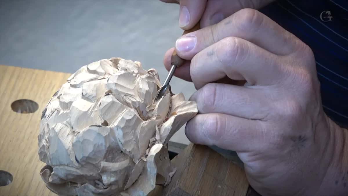 One hand guides a slim gouge into the side of the flower