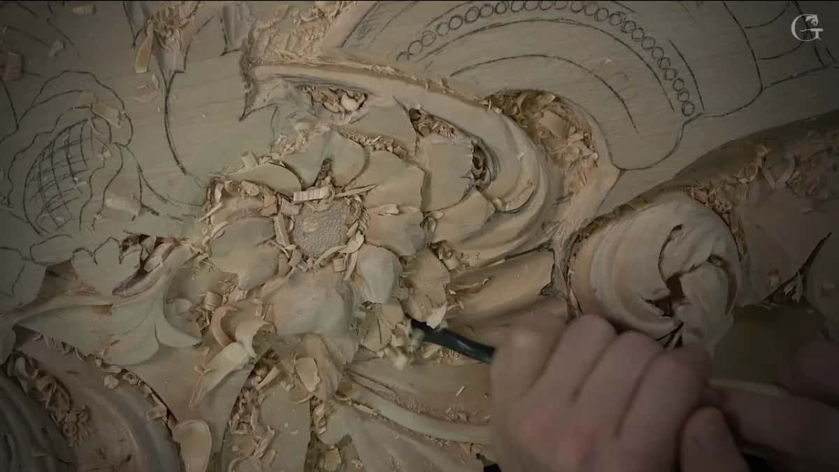 Hand guiding a small dark handled gouge under the flower petals