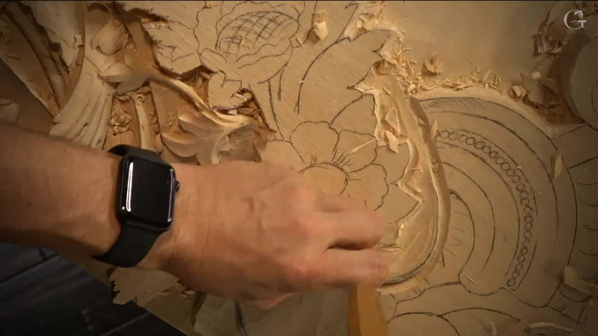 A hand works a gouge beside the flower drawing.