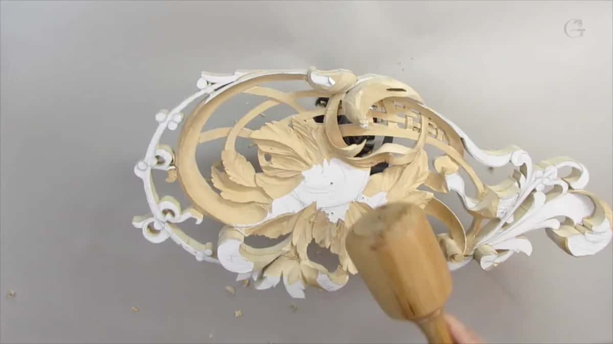 Light wood mallet swinging above the panel, chips on the bench and a hand at right