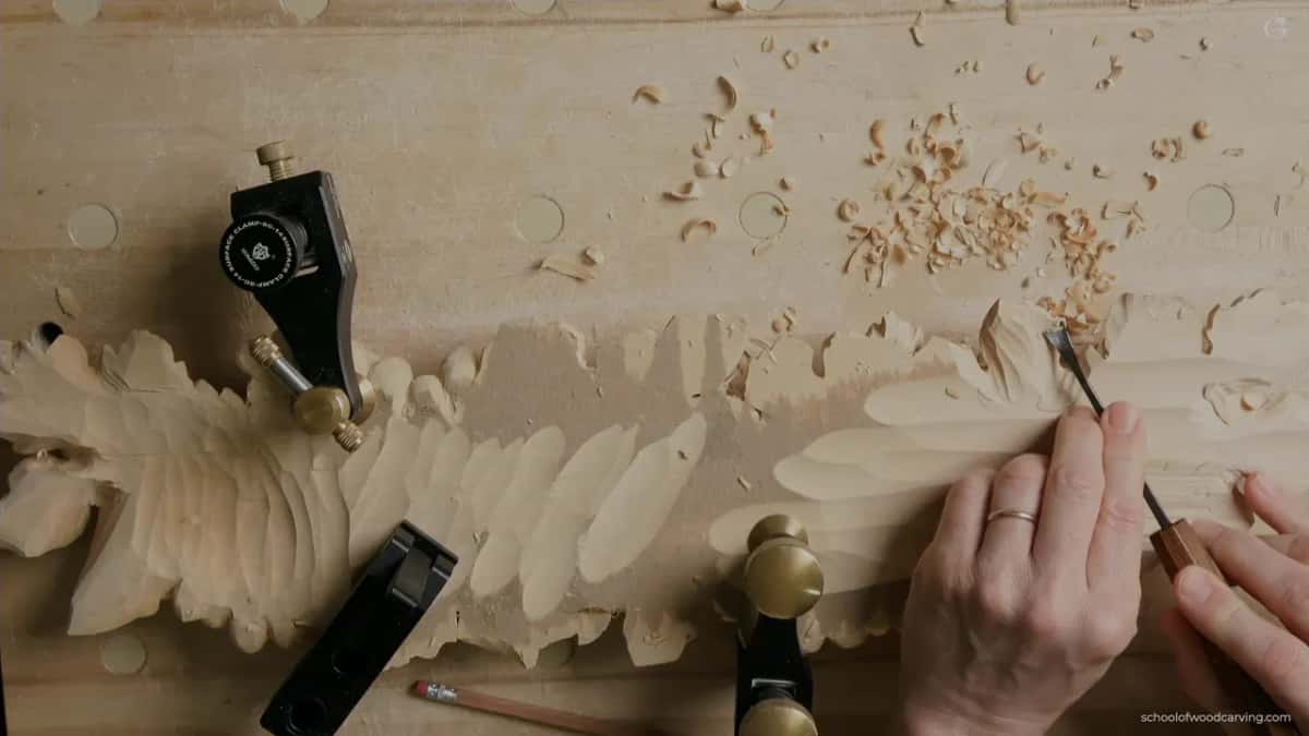 Clamped face down, a narrow gouge at work near the right end, chips scattered past it