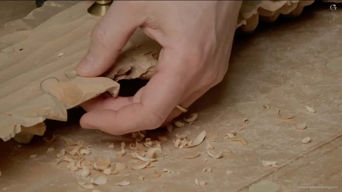 Hand lifting one end, curls of wood on the bench
