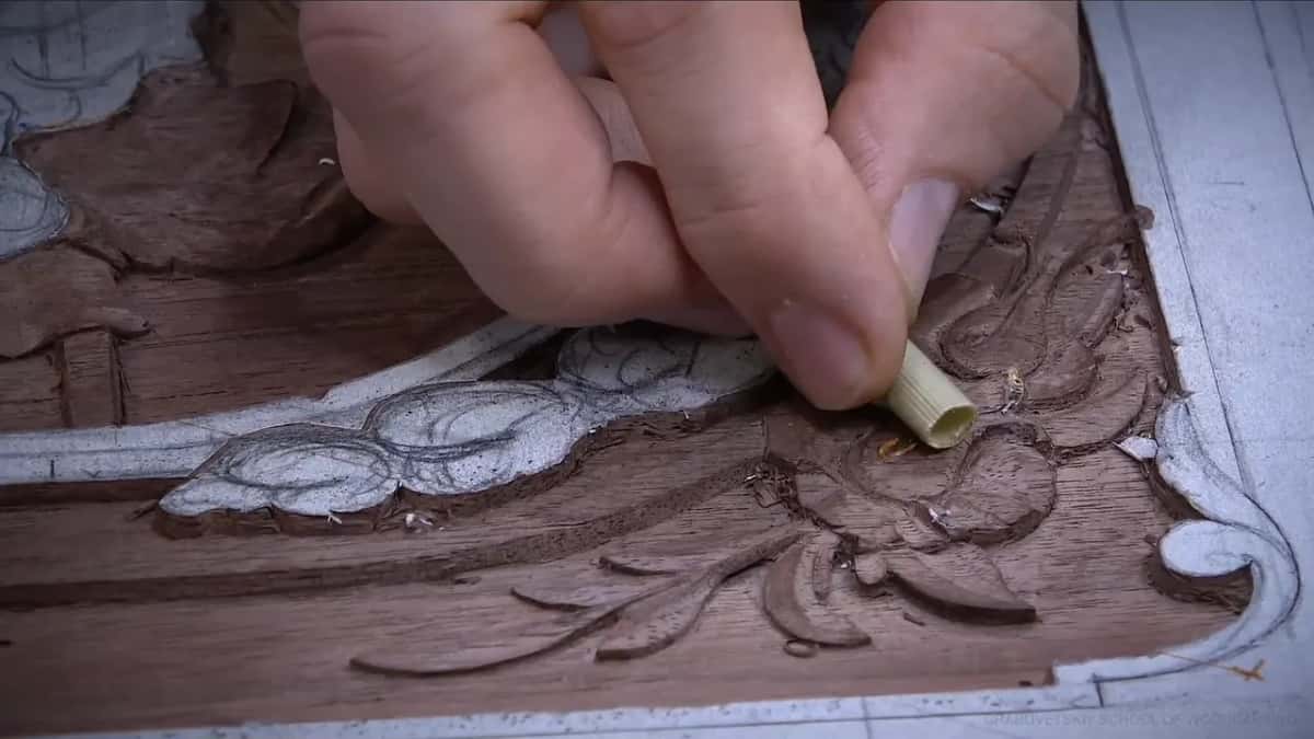 A hand pushes a pale reed stem down on the carved leaves