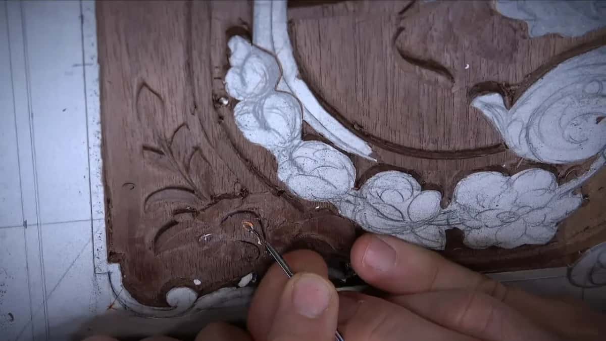 Fingers low on the board steer a fine veiner into the carved flower by the corner scroll