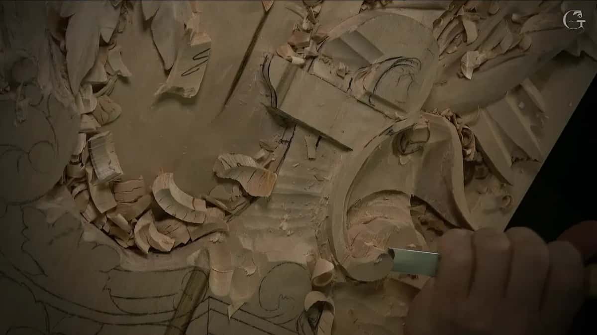 Close up, a flat gouge pushed across the lowered area beside the volute, chips piled on both sides