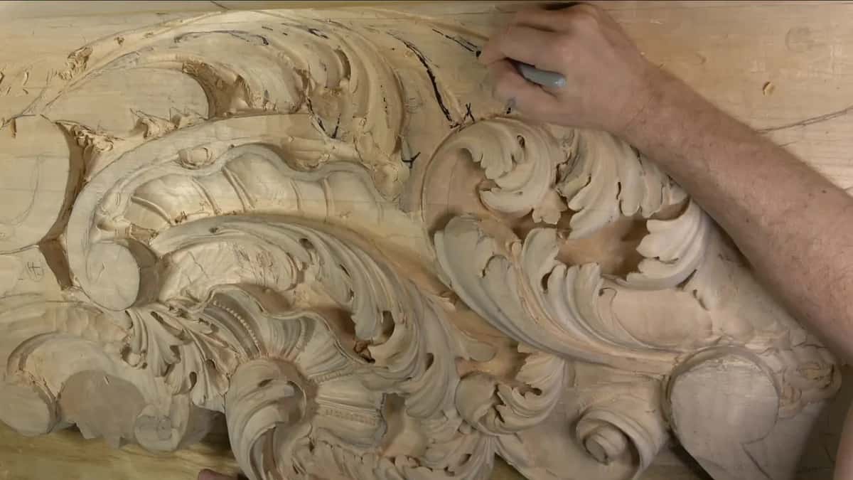 A hand holds a black marker over the flat wood above the carved leaves.