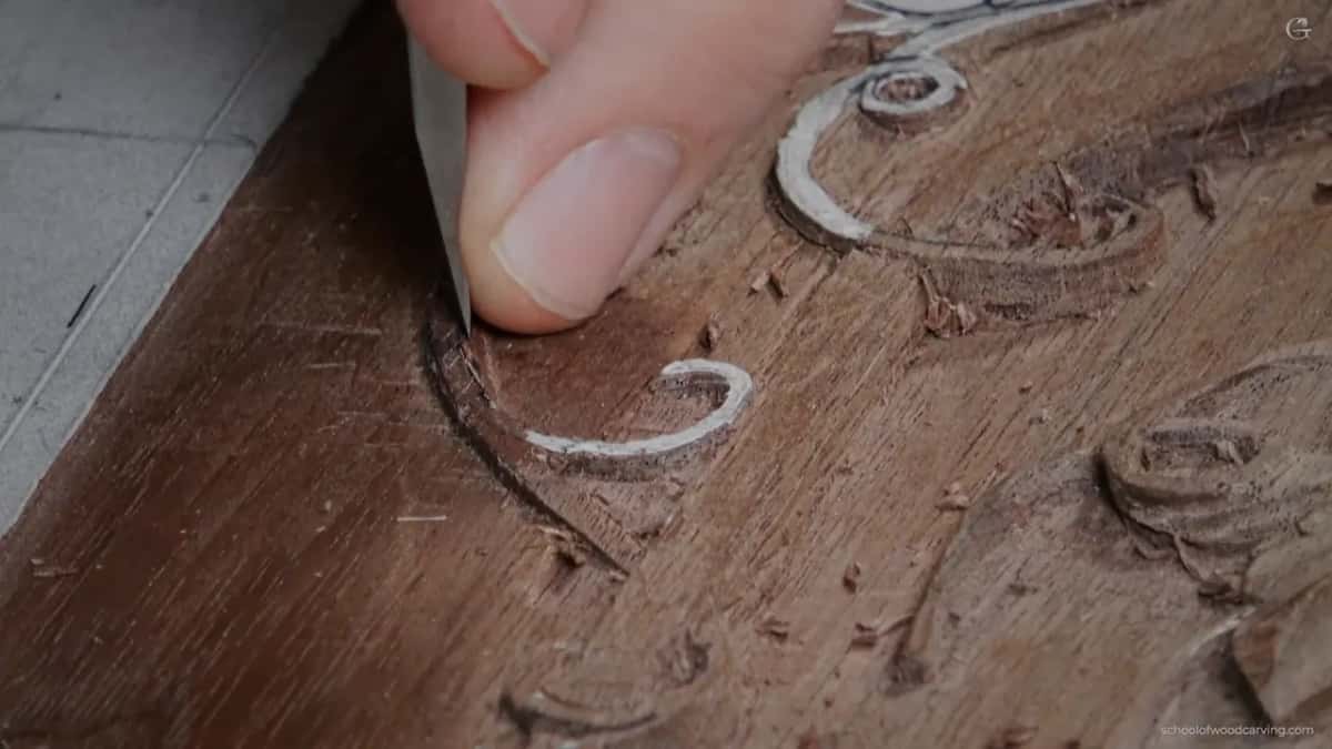 Flat blade under his thumb at a small curl of paper pattern, with dark walnut all around it