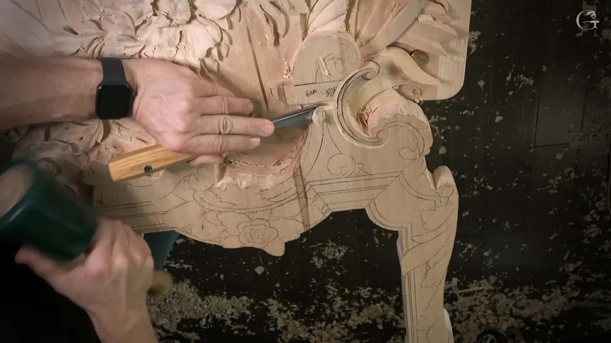 A green mallet comes down on a wide gouge lying almost flat on the panel