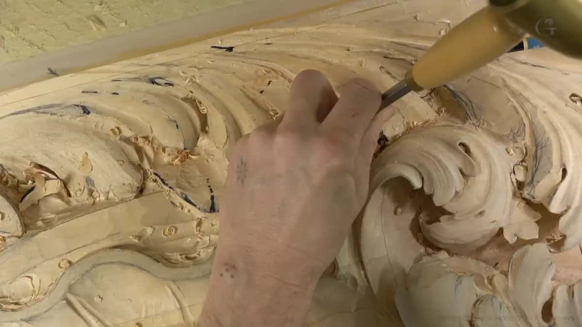 Pale handle angled toward the carved volute, with a blue object at the top right.