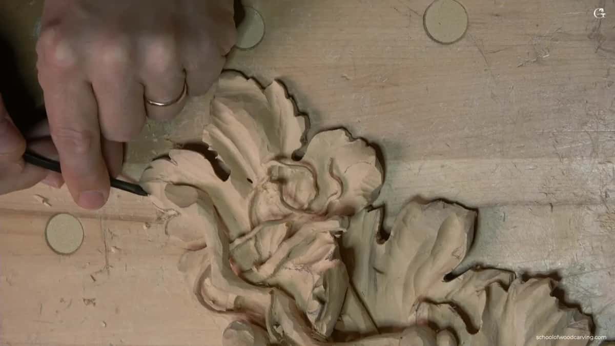 A ring hand brings a dark tool to the corner leaf, seen from the top of the board