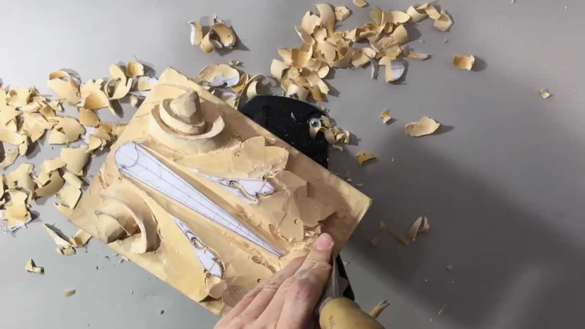 Board at a slant on the vise, chips piled around, one hand at its lower right corner