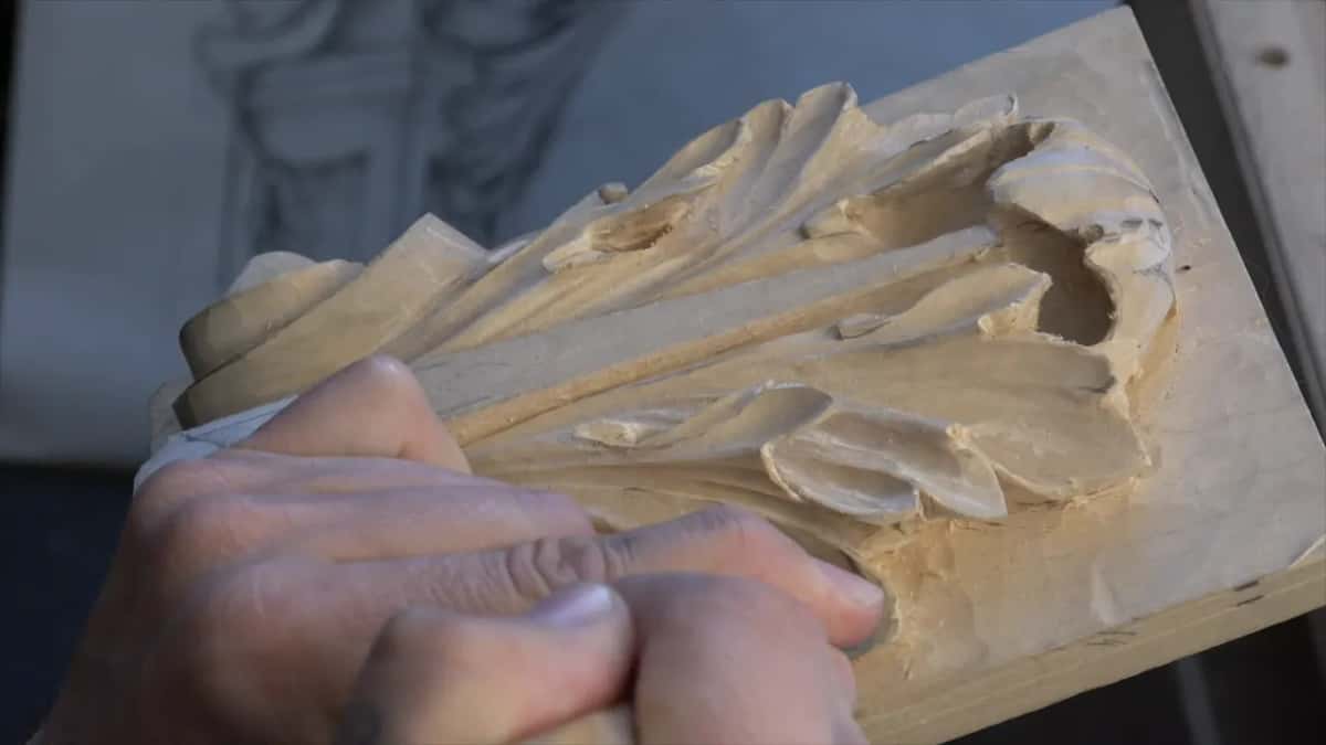 Both hands stacked low on the board near the base of the leaf, a pencil drawing on the wall behind