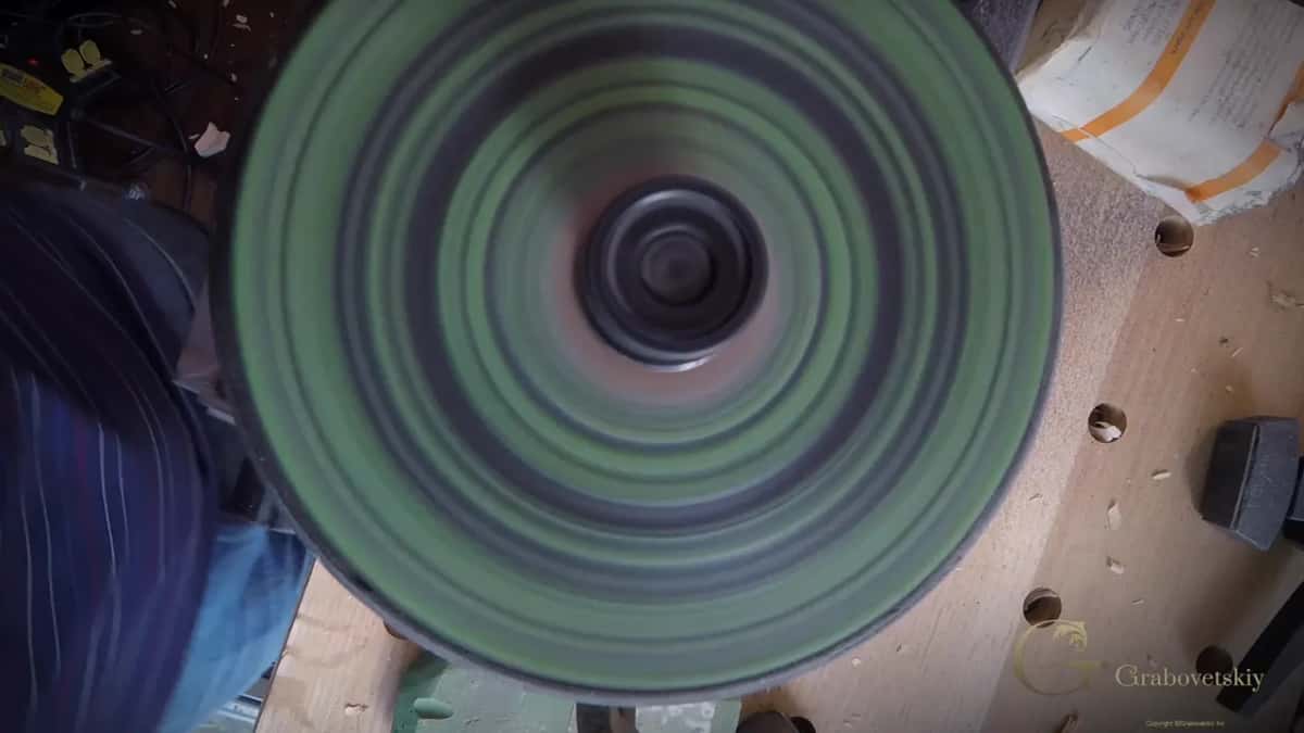 Bright green rings fill the frame as the wheel spins, with shavings scattered across the bench beside it.