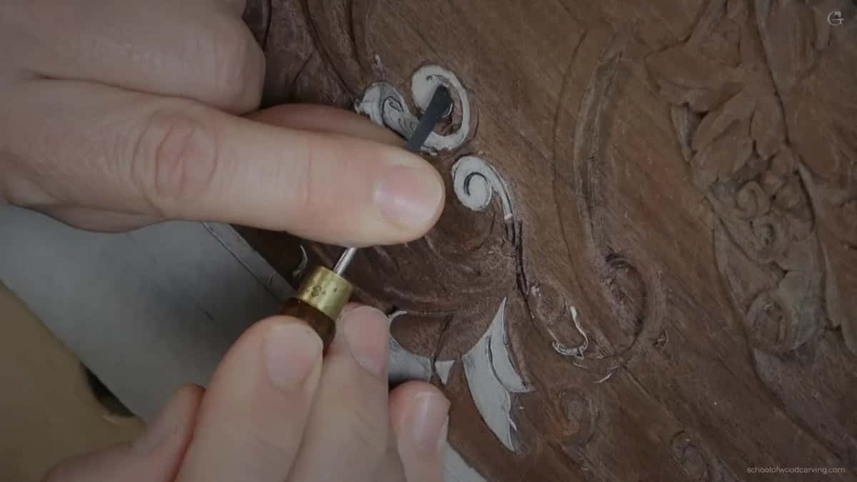Brass ferrule and a dark blade sitting inside the curl of the scroll, his thumb and fingers around the handle