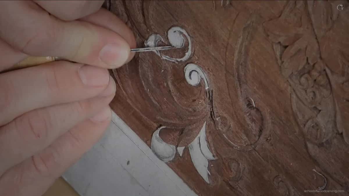 One thin tool held straight up at the edge of the scroll, his fingertips close to the steel