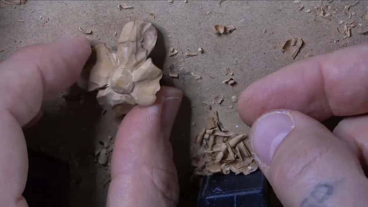 Second filler held up in two fingers, center domed, petals thin and light, shavings on the bench beside it