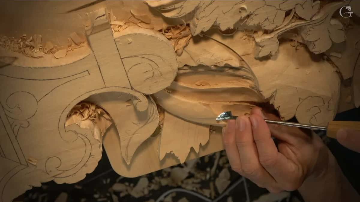 Bent shank of a small tool reaching under the leaf edge, pencil scrolls on the board to the left