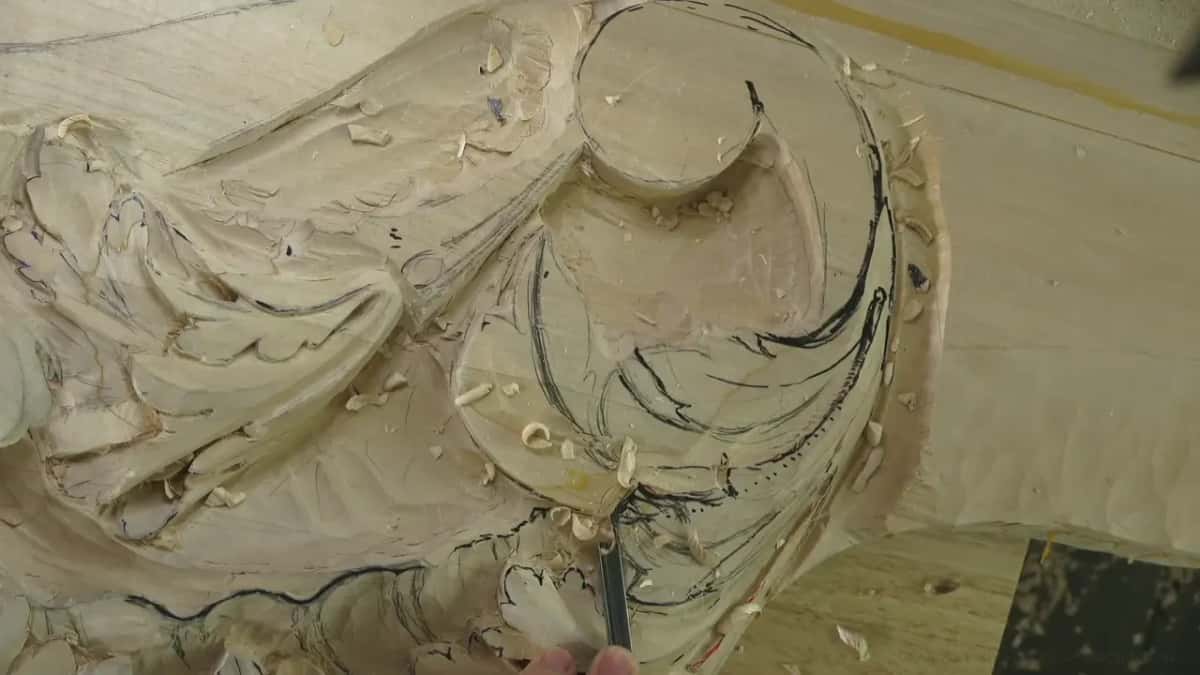 At the foot of the scroll, a small tool tip sits in the wood under fine chips.