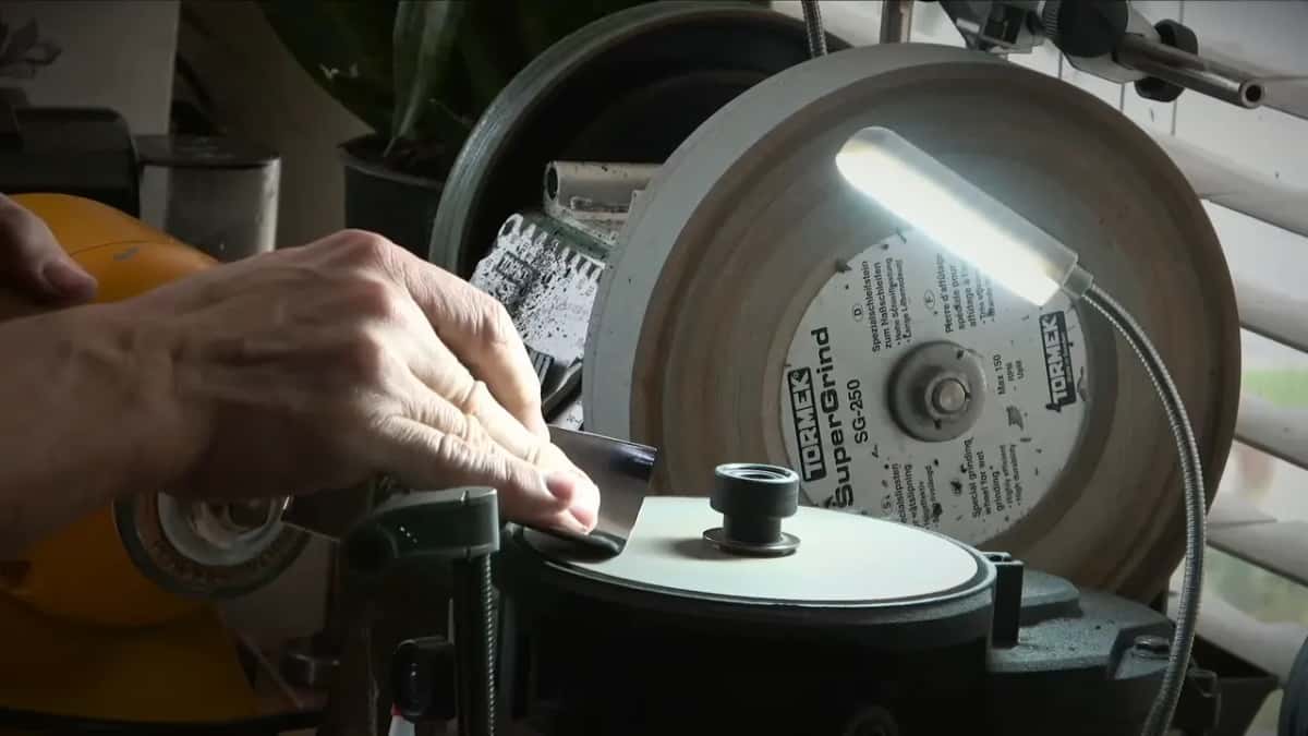 A gouge clamped in a jig over a flat disc, a Tormek wheel standing behind