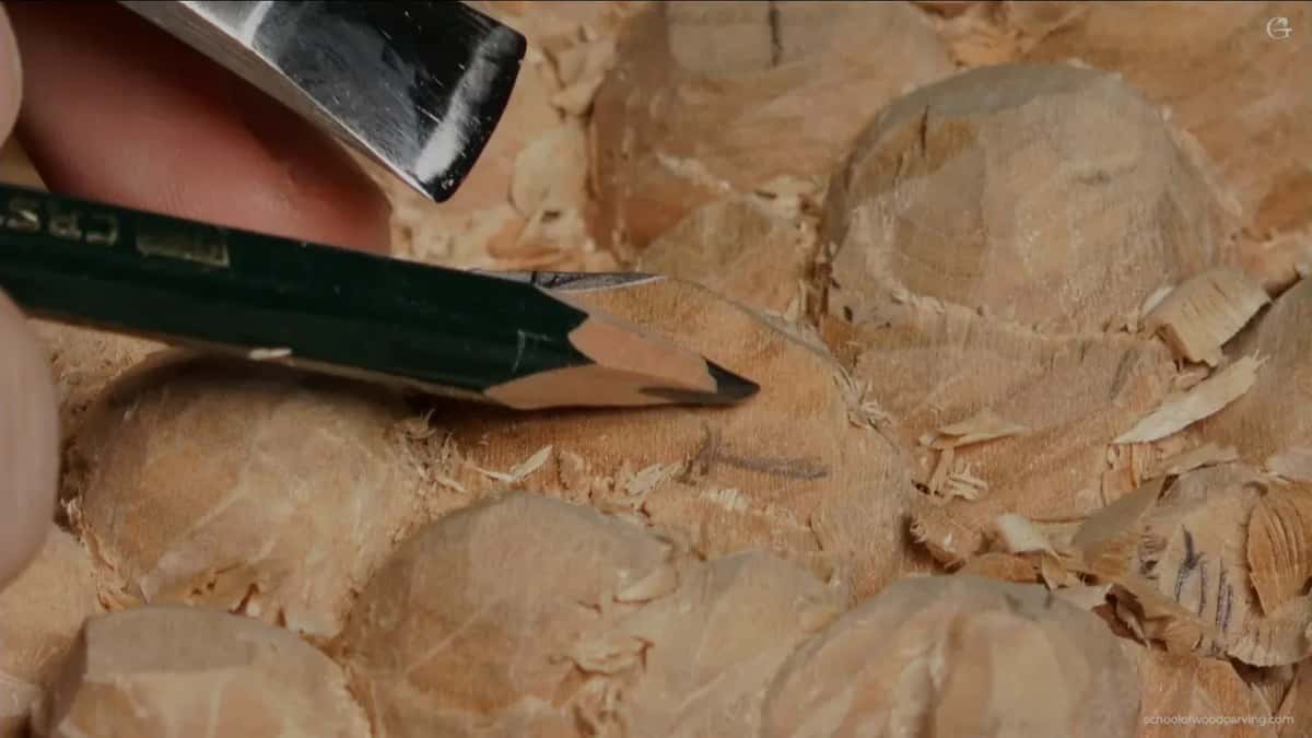 Green pencil and a gouge blade held just over faceted grapes, pencil lines on the wood