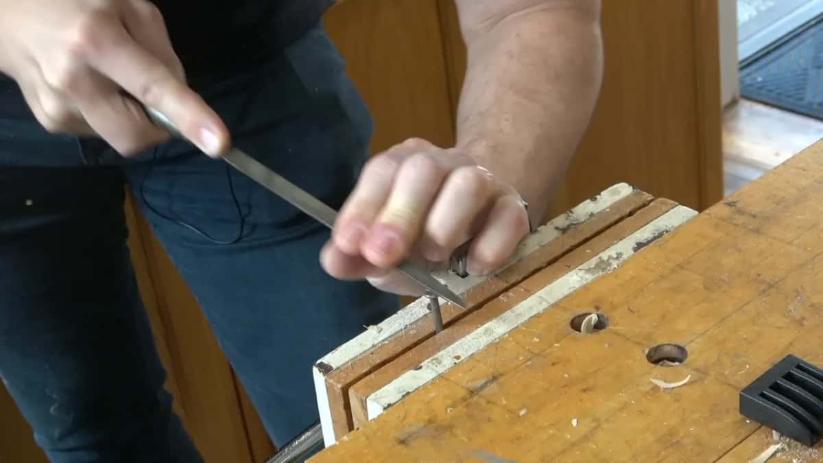 Nail held in the vise while a file cuts into the head