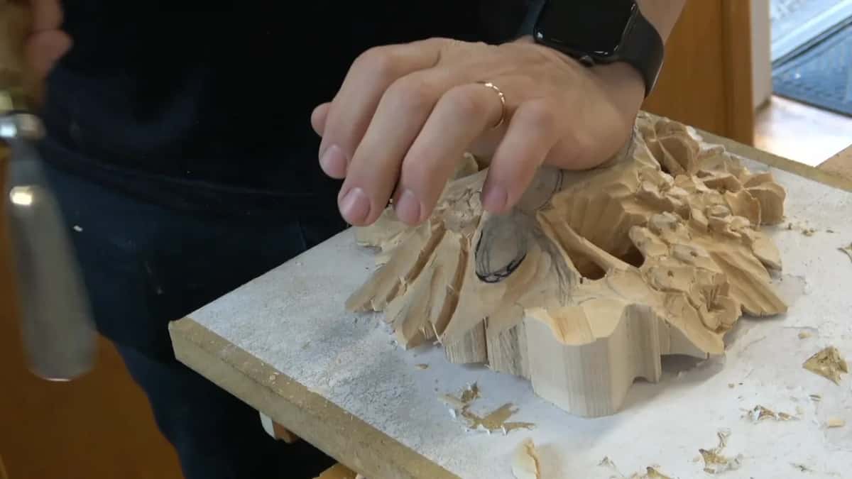 One hand flat on the carved face, the other holding a gouge