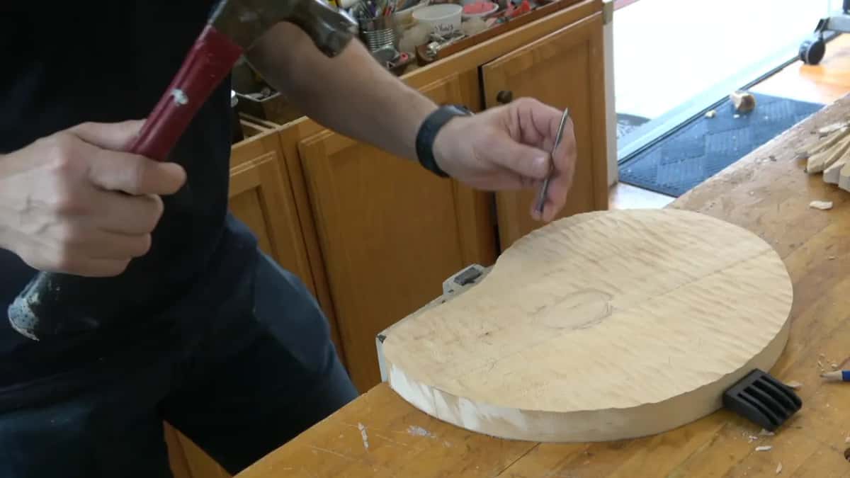 Hammer up in one hand, the nail in the other, over a board already textured around a clean oval