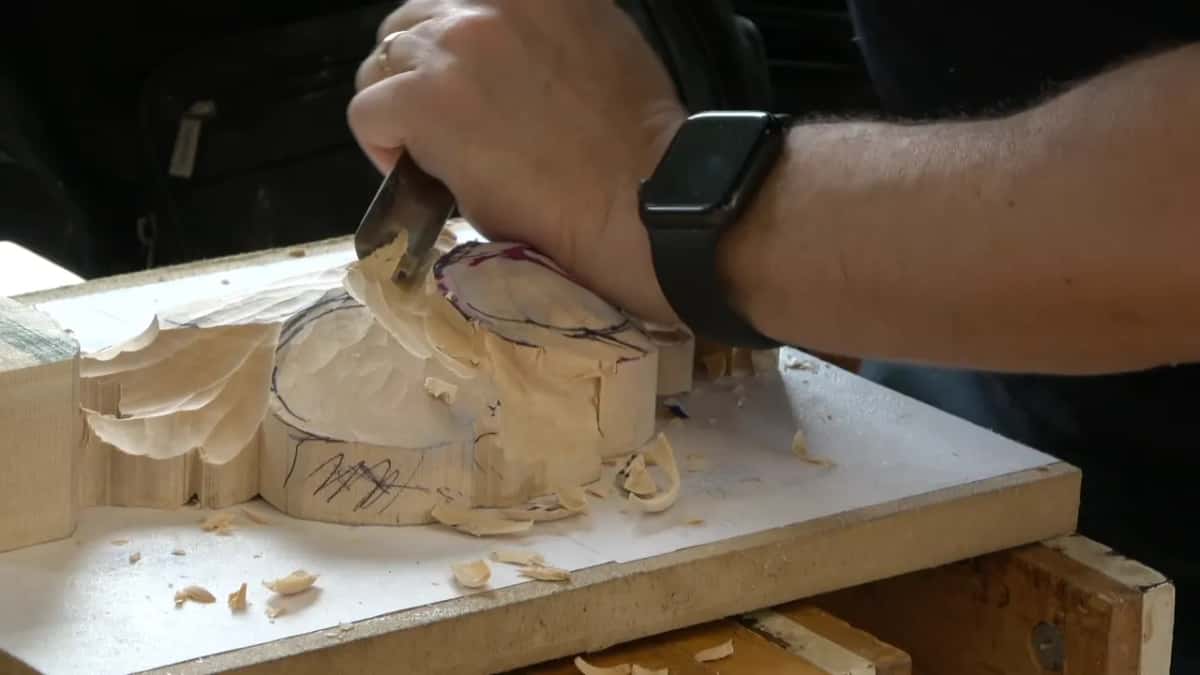 Right hand drives a gouge down the rim of the round tulip block, chips stacked on top
