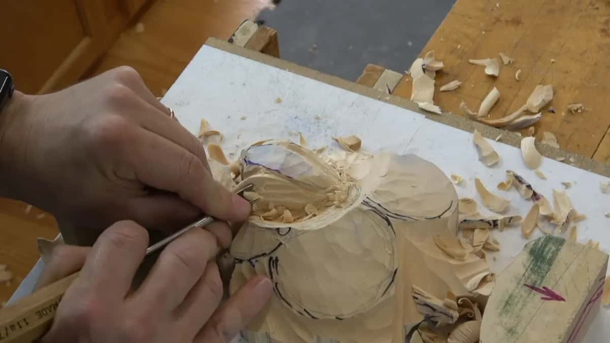 Two hands guide a slim tool under the curled petal edge, a label on its handle