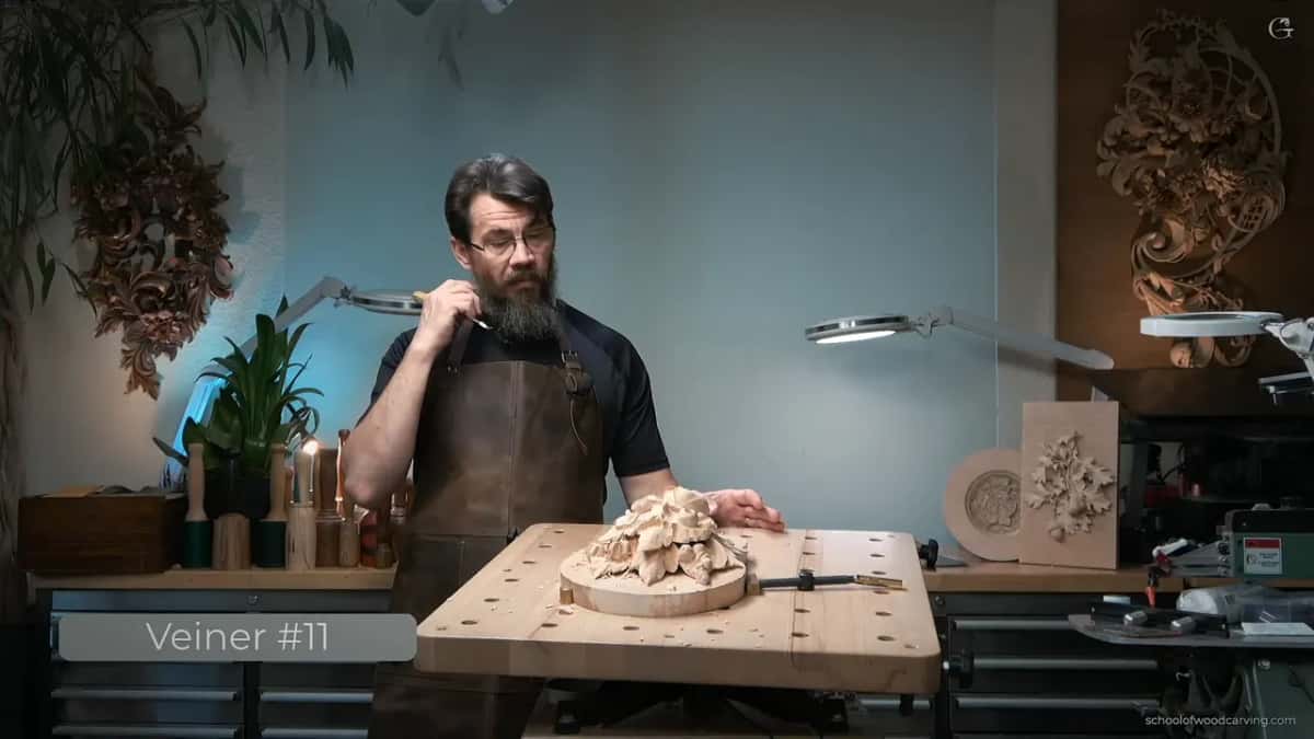 At the bench, holding up a tool while the caption on screen reads Veiner #11