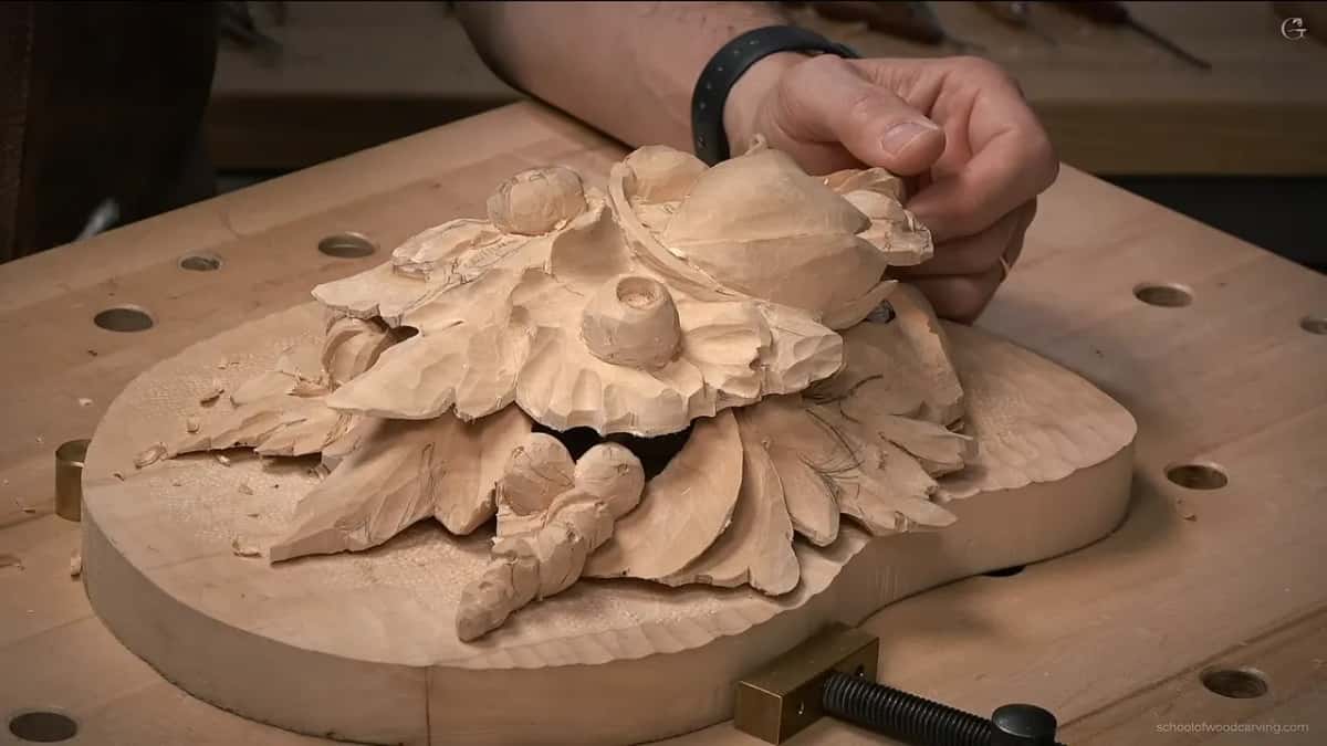 Low across the bench, the carved flowers sit on their round base board, a clamp in front and one hand on top