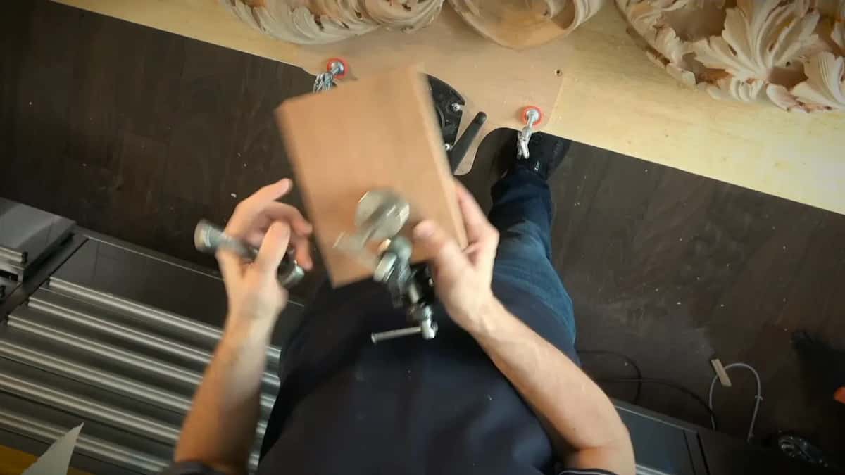 Both hands lifting the block, a Veritas plate on one face and a clamp vise mounted on the other