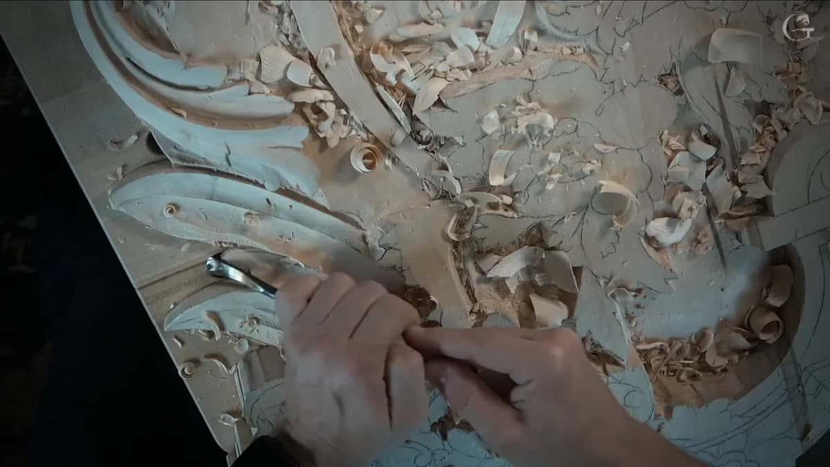 Both hands guide a small gouge in under the edge of the leaf