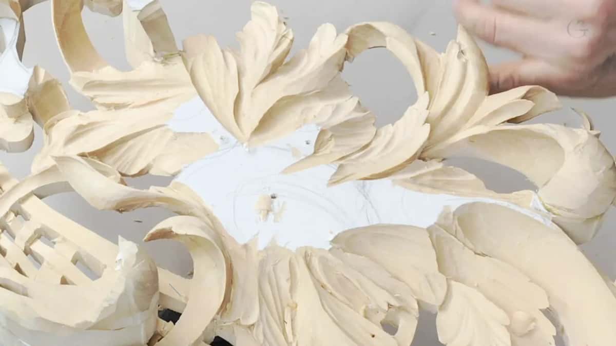 One hand rests over the carved leaves and the white paper at the center