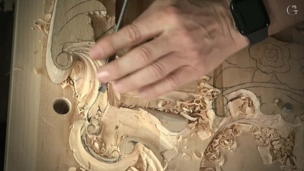 Fingers guide a narrow gouge along the leaf where it runs in close beside the curl