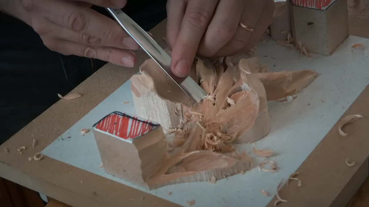 Two hands work a long gouge through a hollow while curls of wood pile up around it